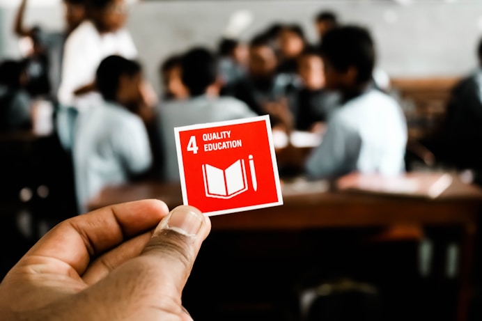 Hand holding a red square with 'QUALITY EDUCATION' underlining the need for equitable access 