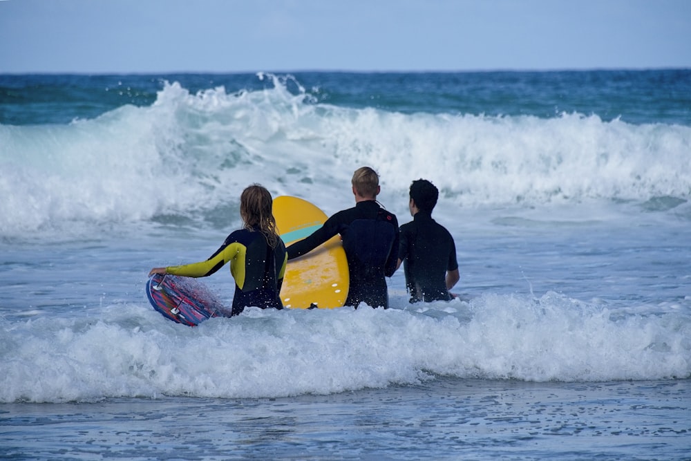 2 men in black wet suit riding yellow and black surfboard on sea waves during daytime
