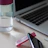 Close-up of a pastel pink stainless steel bottle on a wooden desk next to notebooks and a laptop.