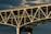 A large, sturdy bridge with complex lattice work and structural beams, showcasing its engineering design. The bridge has an industrial look, with overhead clouds creating a dramatic background.