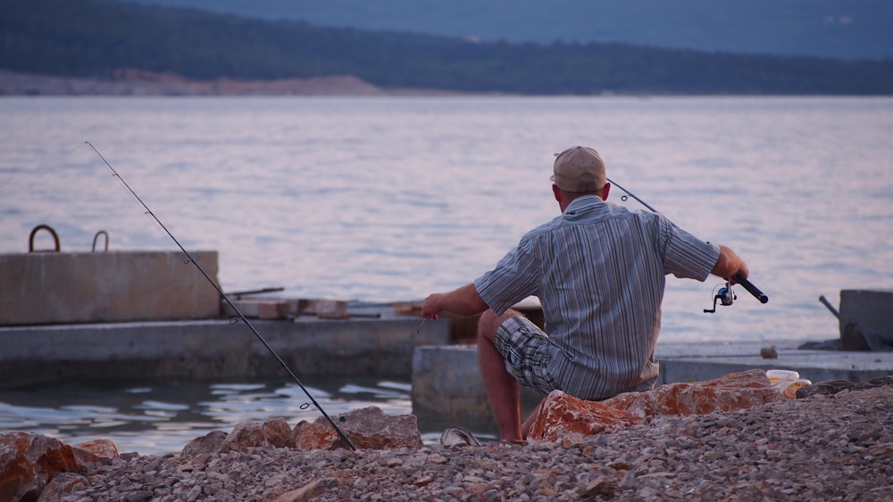 man in blue and white stripe dress shirt sitting on gray concrete bench near body of during