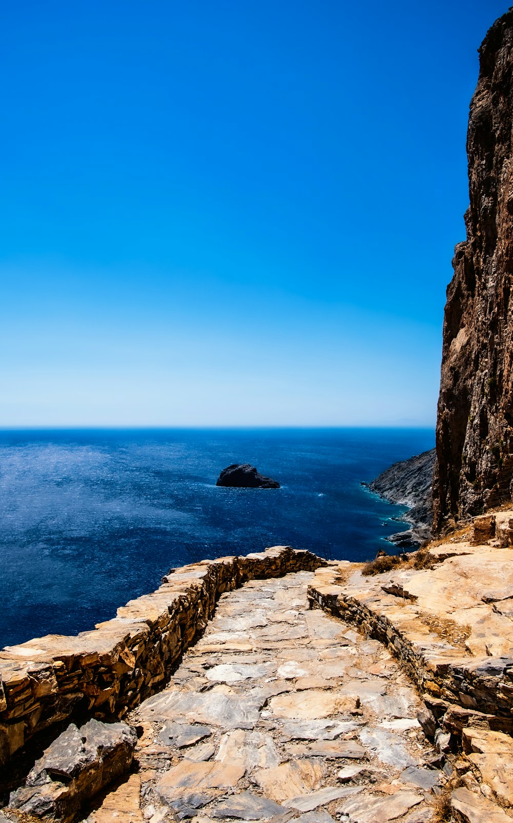 brown rocky mountain beside blue sea under blue sky during daytime