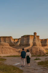 A couple walking hand-in-hand through a sun-drenched terracotta-colored landscape.