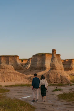 A couple walking hand-in-hand through a sun-drenched terracotta-colored landscape.