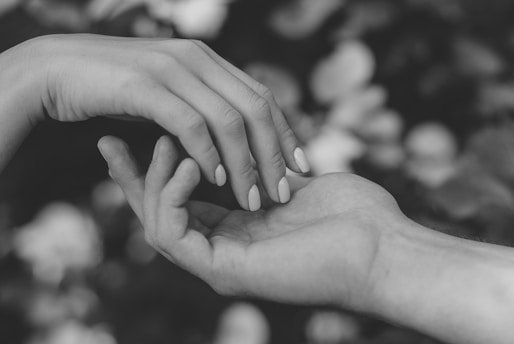 Two hands gently reaching toward each other against a blurred natural background.