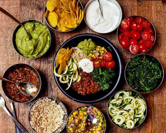 A vibrant bowl of colorful, fresh vegetables and grains arranged beautifully on a rustic wooden table.