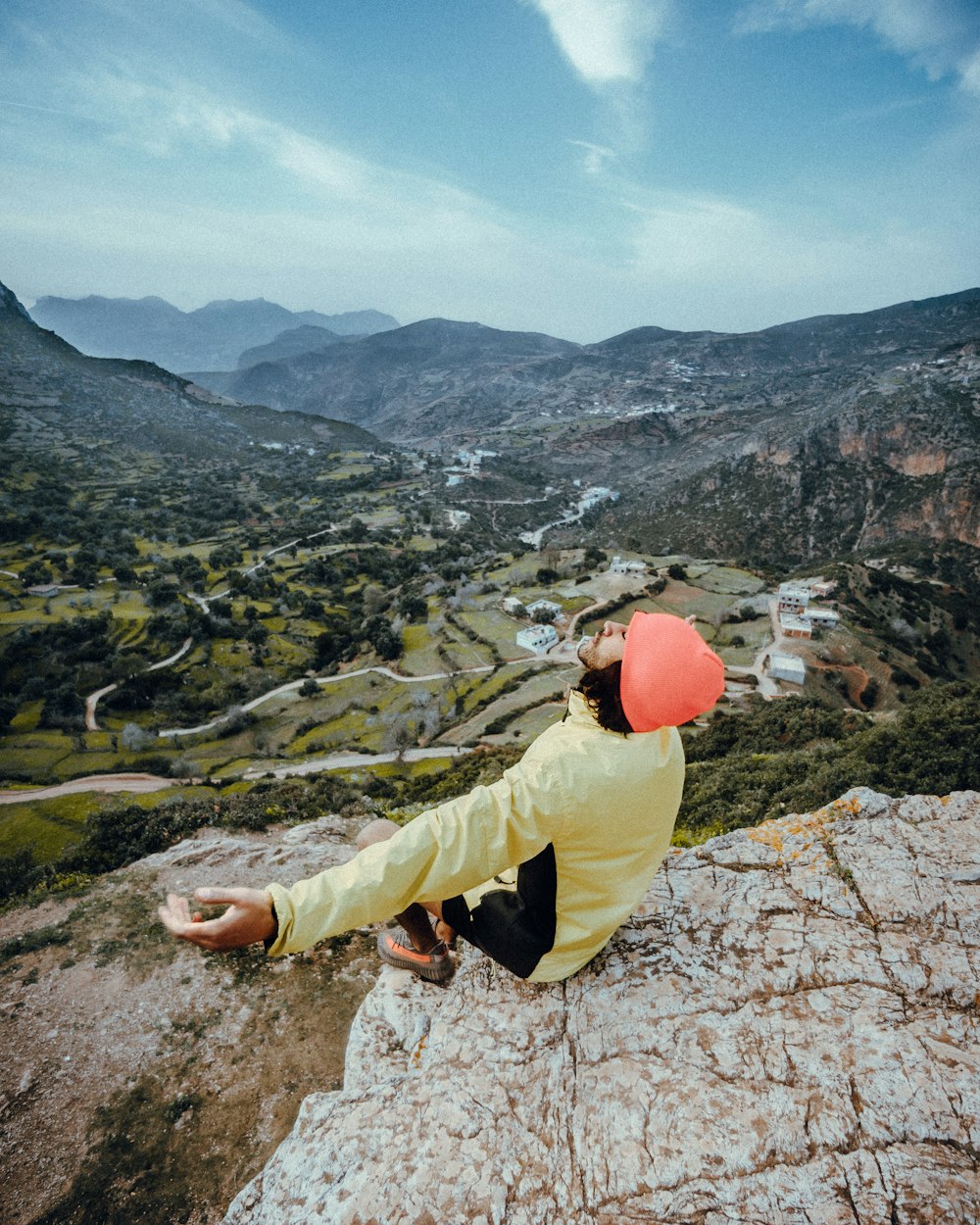 man in yellow jacket and brown pants sitting on rocky mountain during daytime