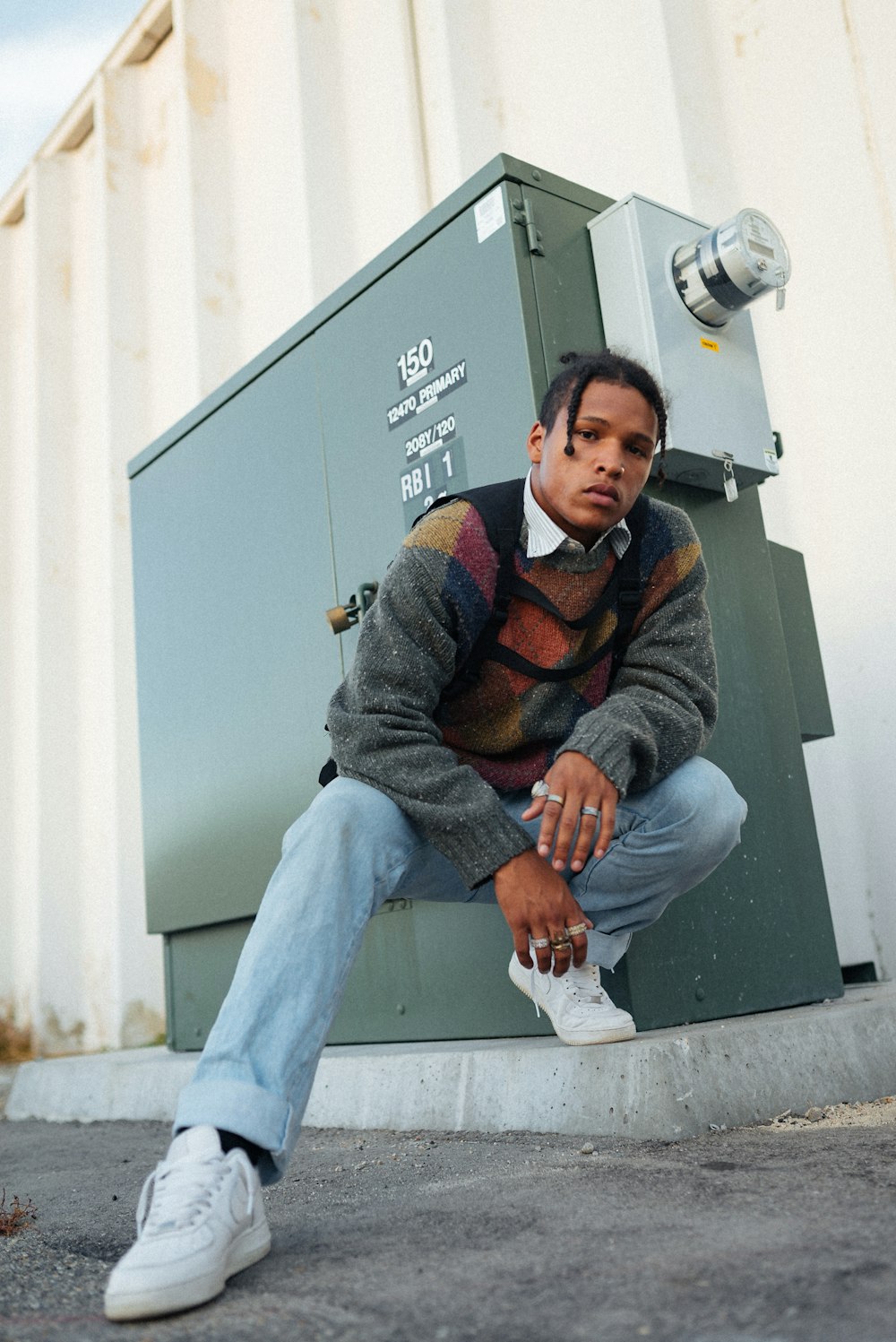 man in gray and orange sweater and blue denim jeans sitting on gray concrete wall during