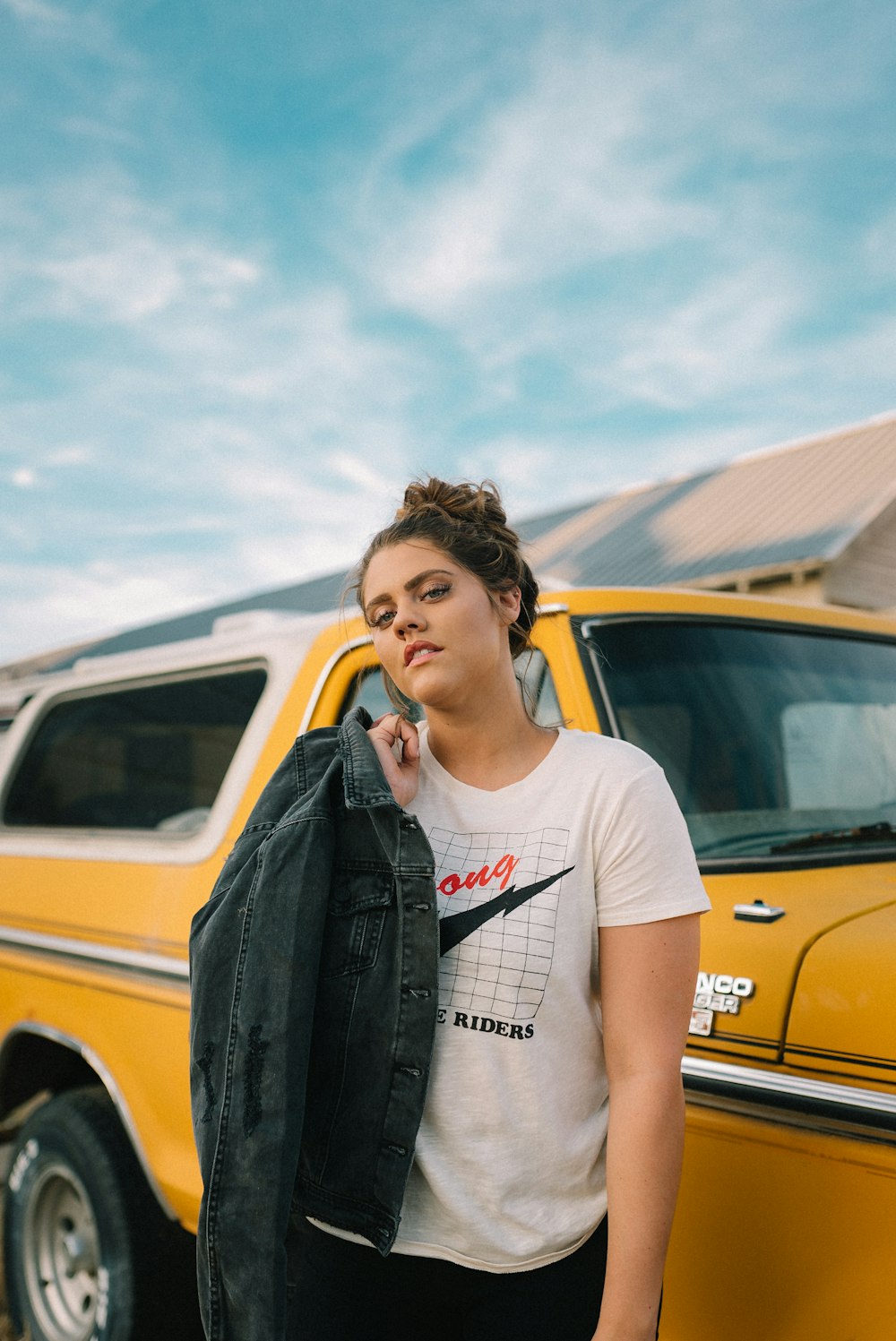 woman in white crew neck t-shirt and black leather jacket standing beside yellow car during