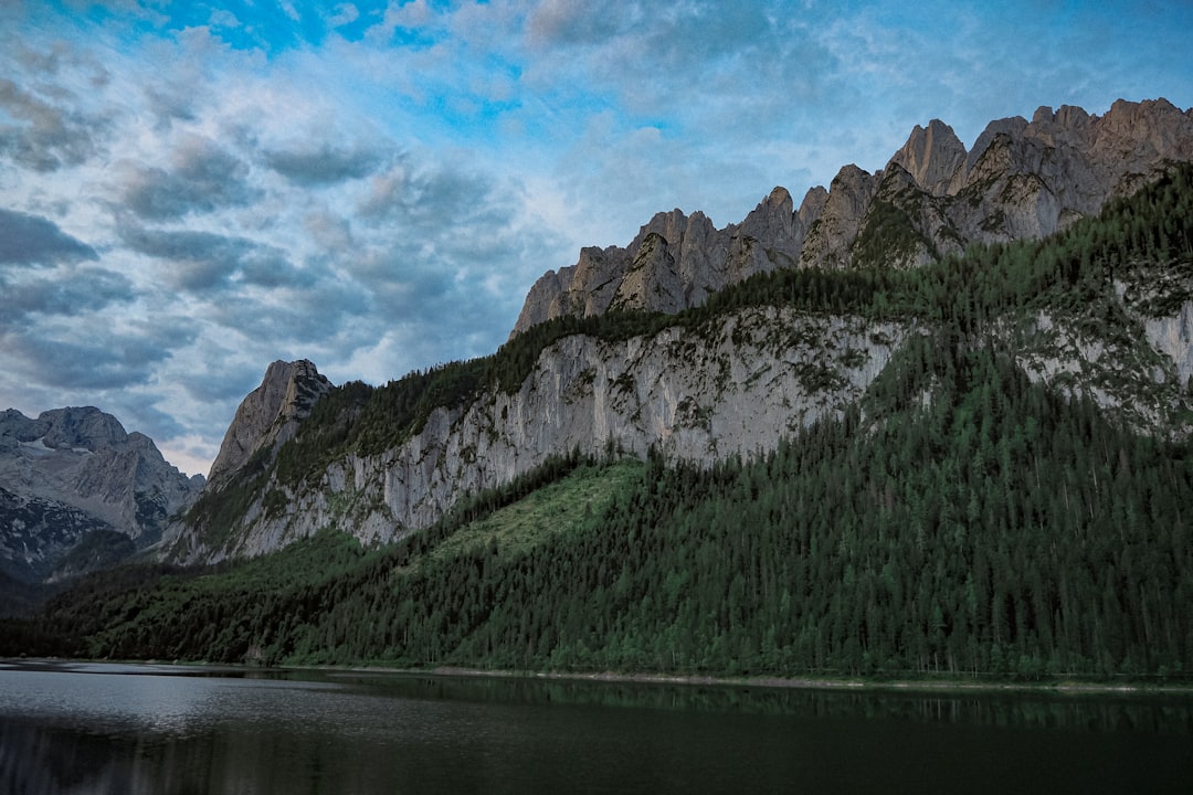 green and gray mountain beside body of water under cloudy sky during daytime