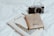 A notebook with an illustration of Big Ben and the word 'London' lies open on a white surface. A vintage-style camera sits adjacent to the notebook, angled slightly towards it. On top of the notebook is a beige passport holder with the words 'Never Stop Exploring' printed on it.