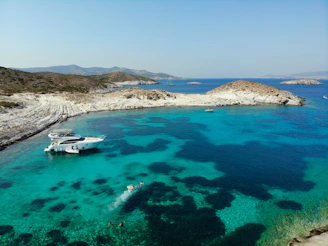 white boat on blue sea water near brown mountain under blue sky during daytime