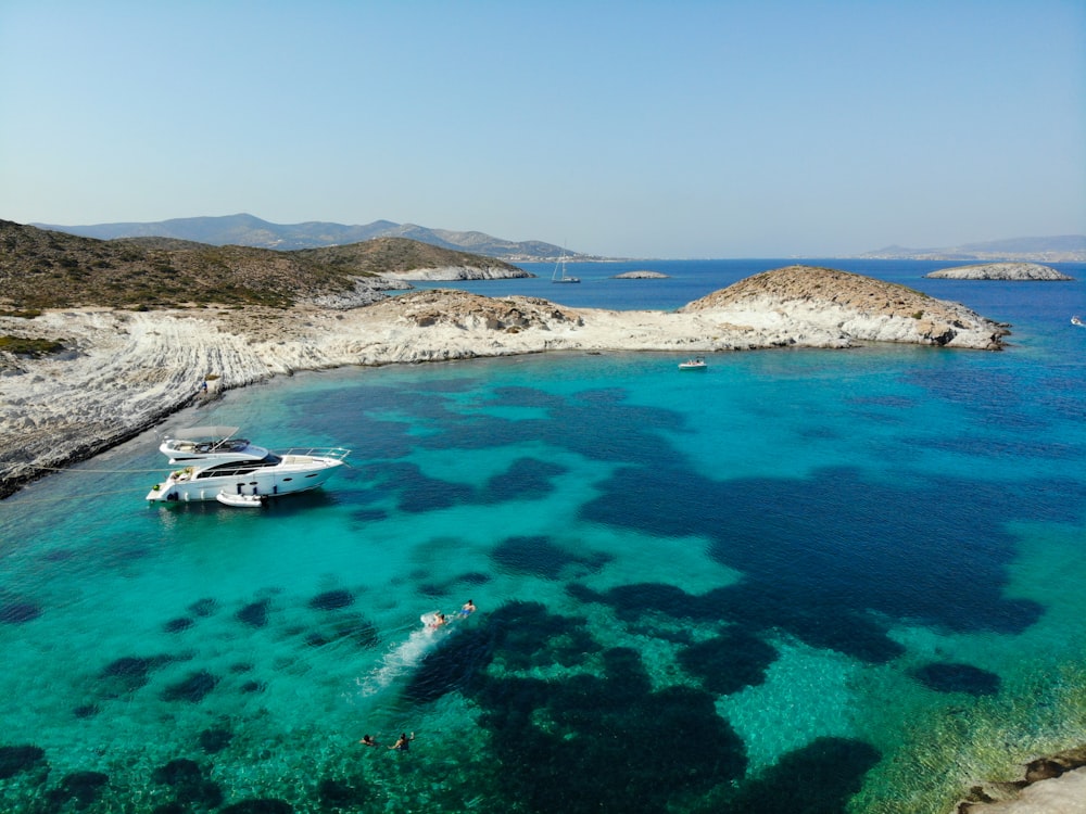 white boat on blue sea water near brown mountain under blue sky during daytime