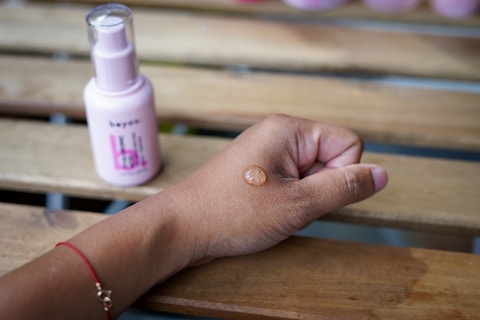 a woman's hand holding a bottle of sunscreen on a wooden bench