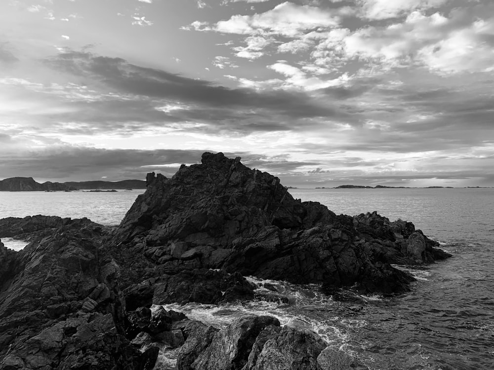 grayscale photo of rocky mountain near body of water