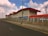 A modern building with a red roof and large secure fence located along an empty road. The sky above is partly cloudy, with scattered electricity poles and streetlights lining the roadway.