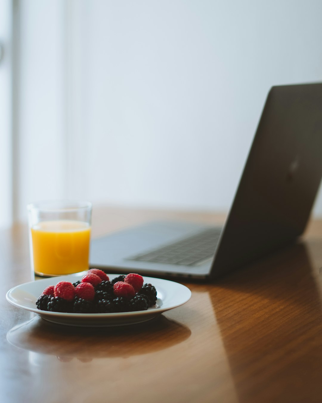 red berries on white ceramic plate beside clear drinking glass with yellow liquid