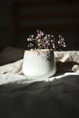A delicate pink ceramic vase holding fresh wildflowers on a sunlit wooden table.