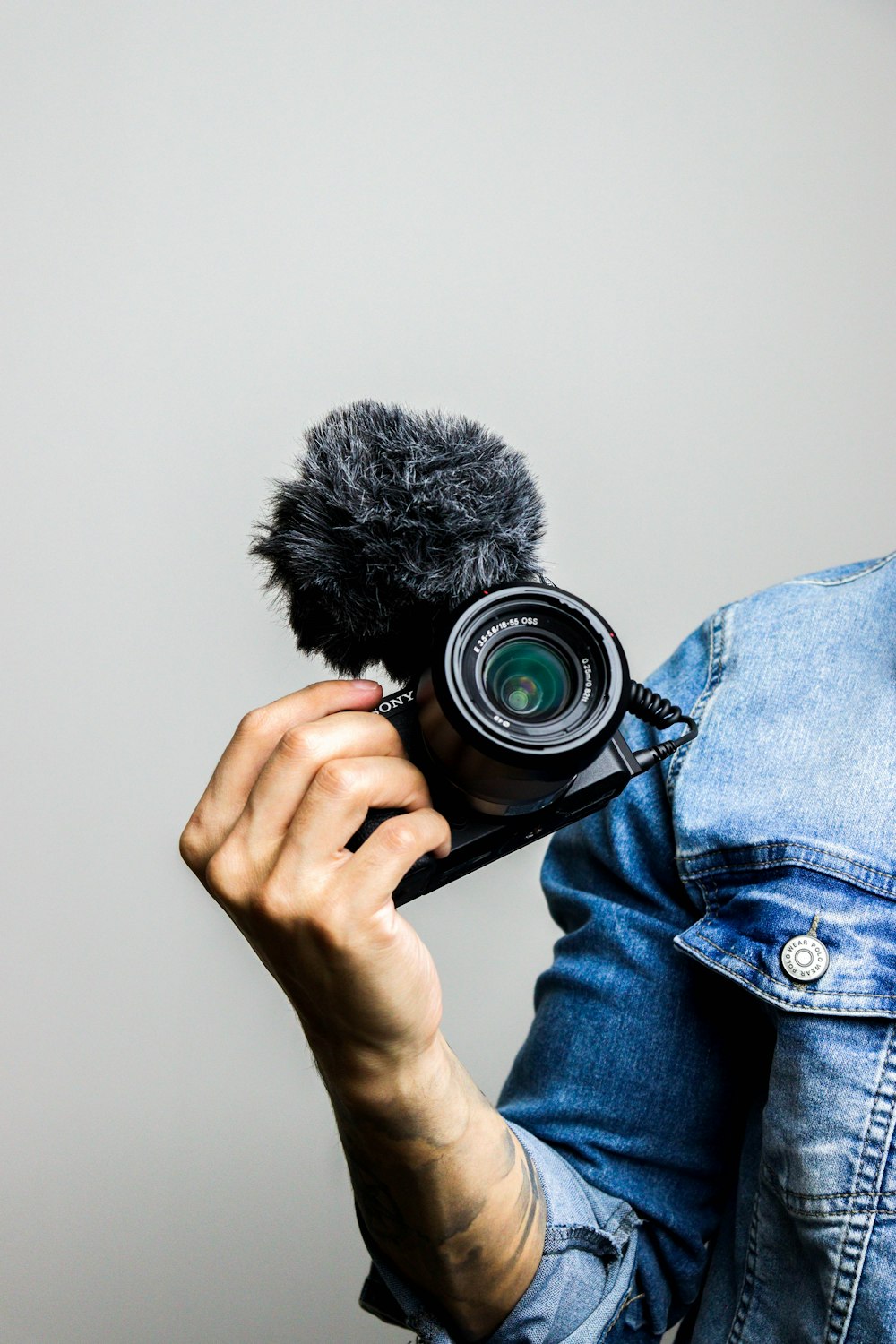 person in blue denim jacket holding black dslr camera