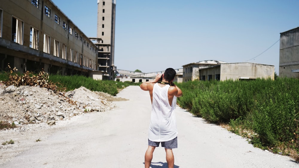 man in white t-shirt and blue shorts standing on gray concrete road during daytime