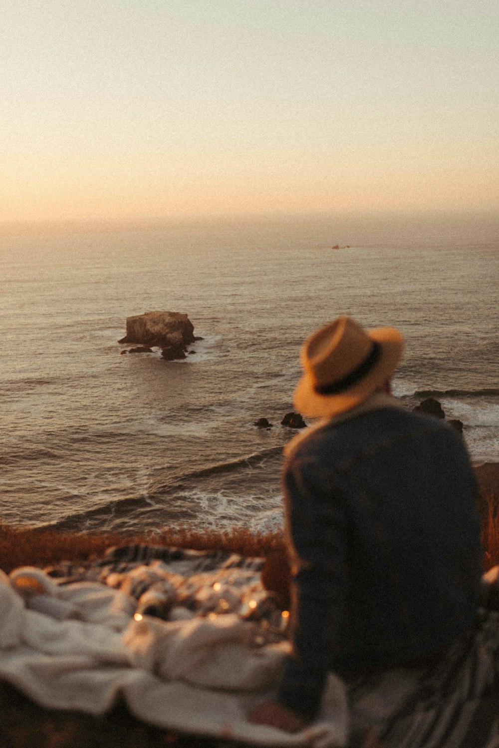 Hombre con chaqueta negra y sombrero marrón de pie en la orilla del mar durante el día
