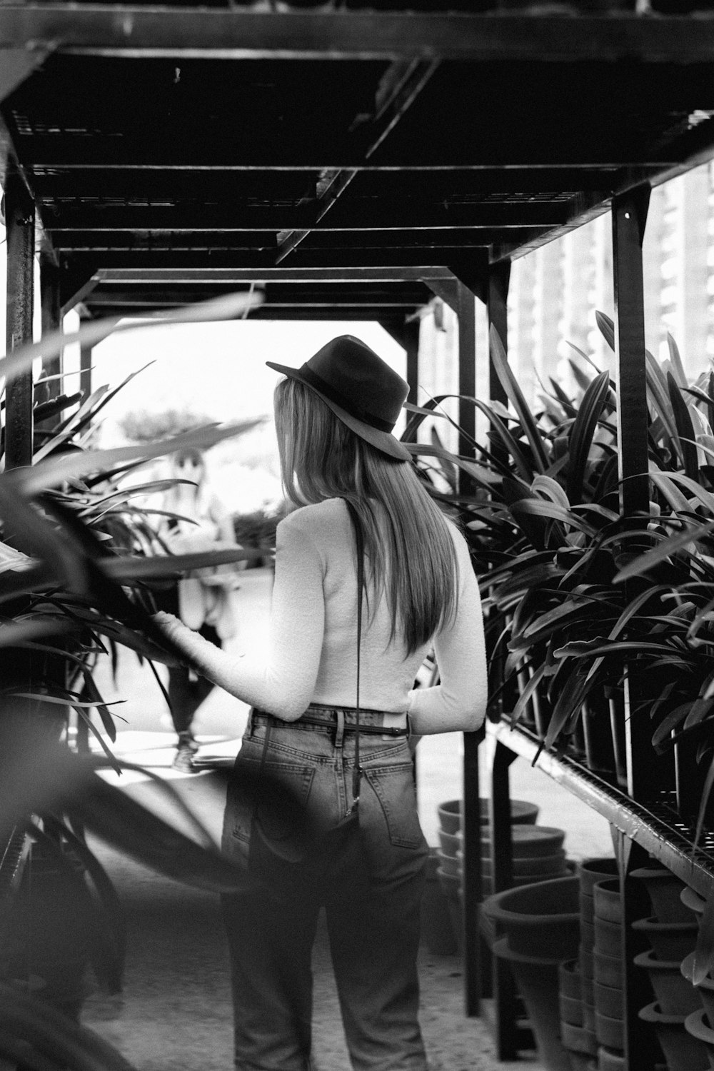 grayscale photo of woman in tank top and denim shorts standing near plants