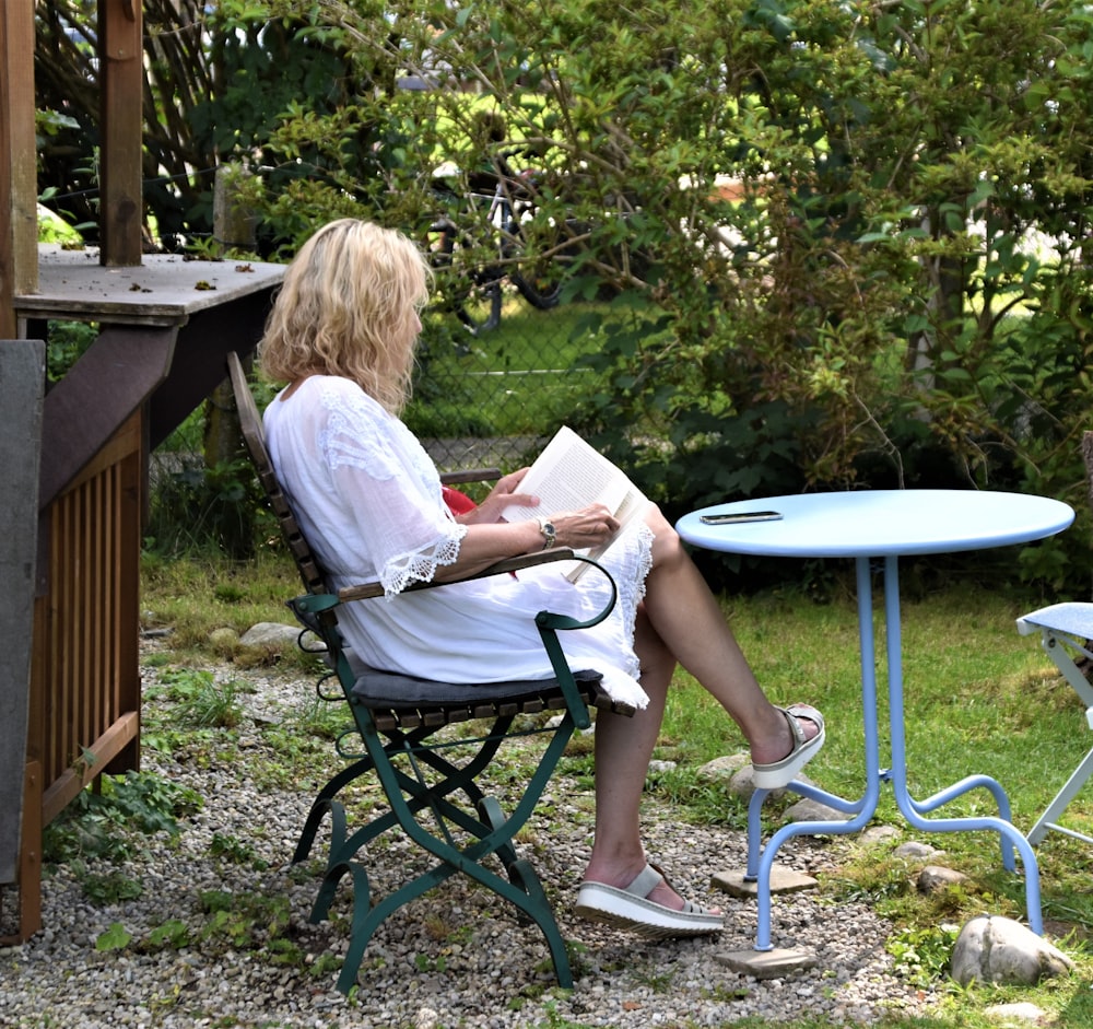 woman in white shirt sitting on black metal chair using macbook
