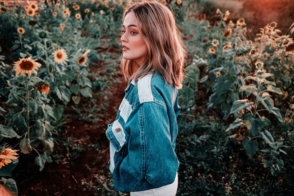 girl in blue denim jacket standing near red flowers