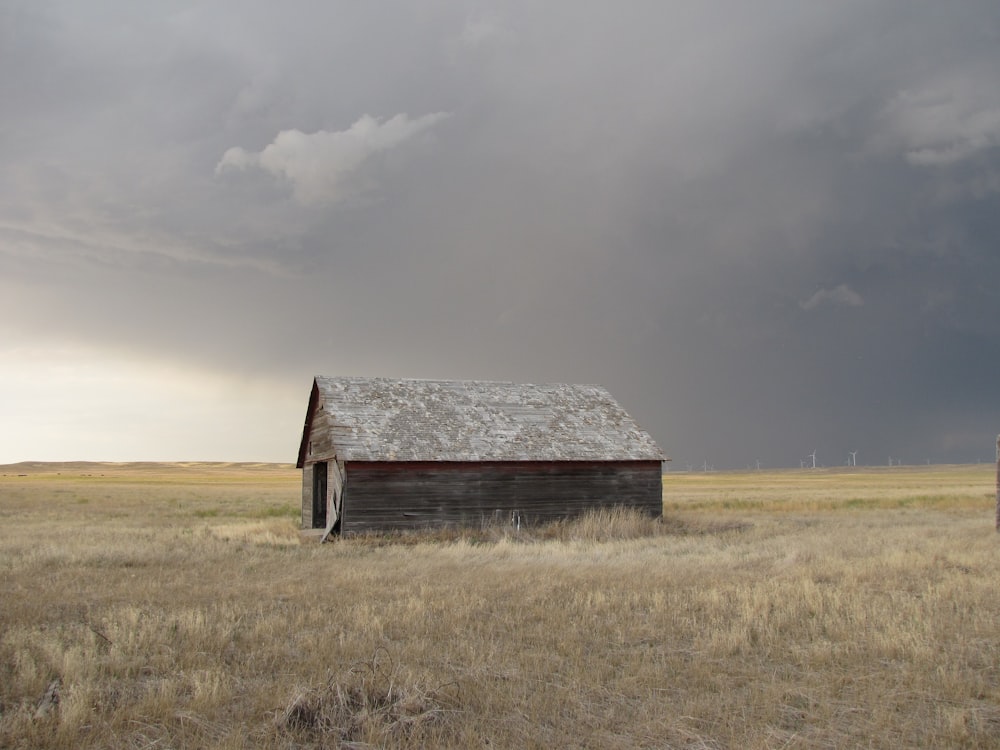 brown and gray wooden house on brown grass field under gray sky