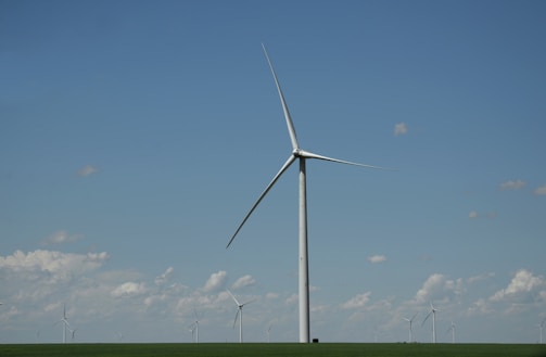 white wind turbine on green grass field under blue sky during daytime