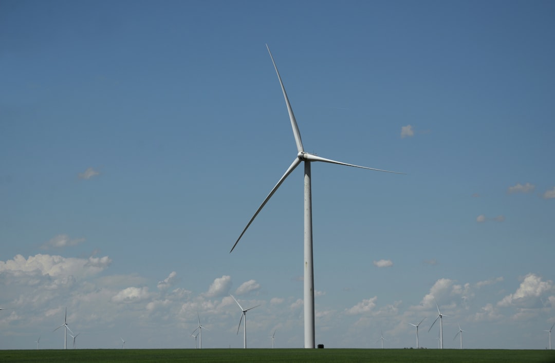 white wind turbine on green grass field under blue sky during daytime