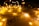 Fairy lights drape softly over a sheet of paper displaying religious symbols and text about love from Romans 5:8. The warm glow of the lights creates a peaceful and inviting atmosphere.