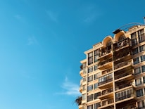 A modern apartment building with balconies and greenery under a clear blue sky.