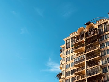 High-rise apartment building with balconies covered in greenery, set against a clear blue sky.