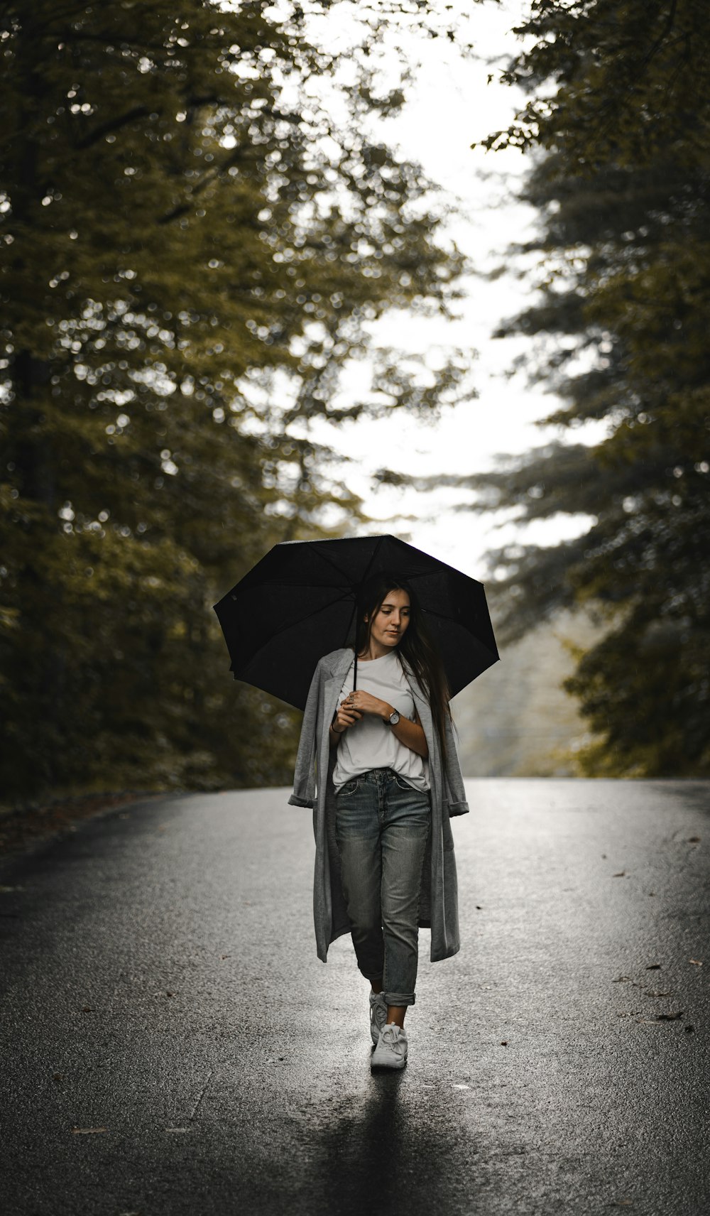 woman in white long sleeve shirt and gray pants holding umbrella standing on road during daytime