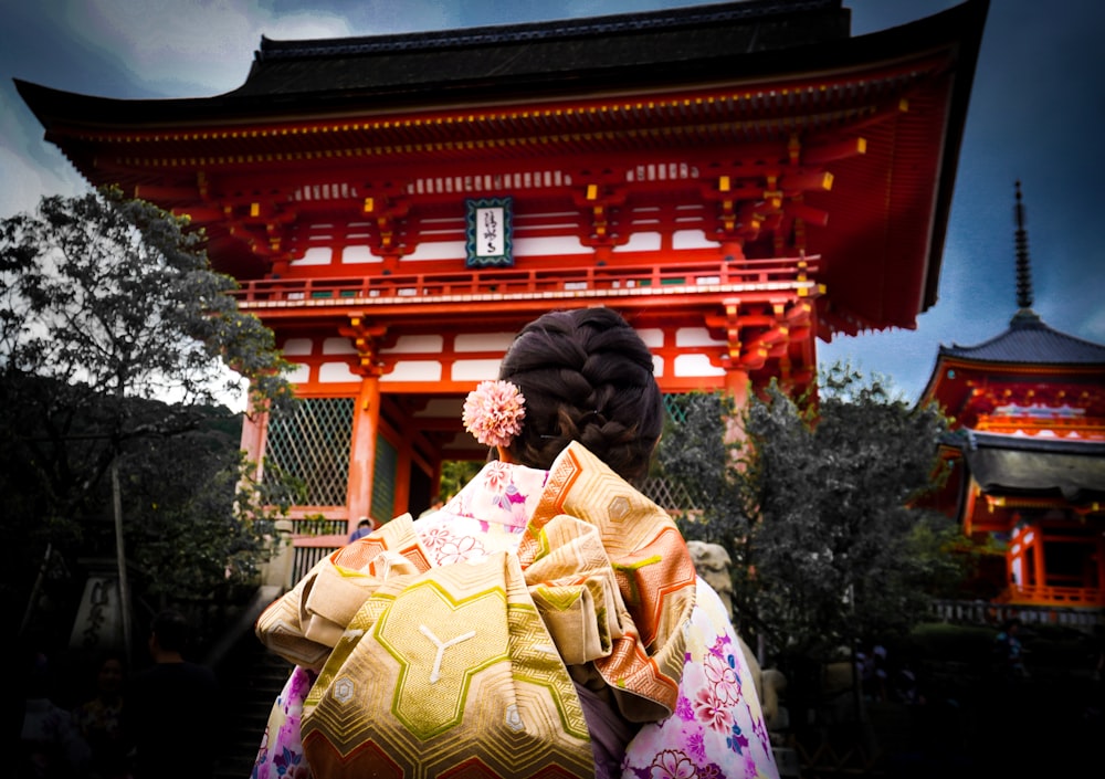 woman in yellow and pink floral kimono standing near green trees during daytime