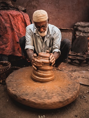 man in white and black stripe dress shirt and brown hat sitting on brown clay pot