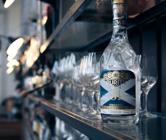 A close-up of a bartender pouring Pinnacle Gin into a glass, with the sea visible through a window behind.