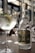 A bottle of Purity Gin 34 is prominently placed on a table, reflecting light with its elegant, faceted design. Next to the bottle is a gin and tonic cocktail garnished with fresh herbs and a slice of lemon, served in a large, rounded glass. The setting appears to be a sophisticated bar or restaurant with blurred backgrounds of glassware and soft lighting, contributing to a refined and classy ambiance.