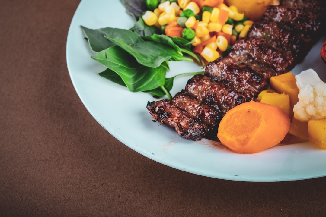 grilled meat with green vegetable on white ceramic plate