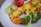 Grilled paneer with a slightly charred surface is served alongside a colorful assortment of vegetables including broccoli, carrots, peas, and corn. A roasted tomato and sliced cucumbers add freshness to the plate.