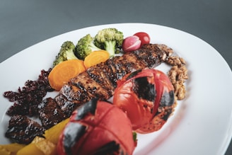 grilled meat with sliced tomato and green vegetable on white ceramic plate