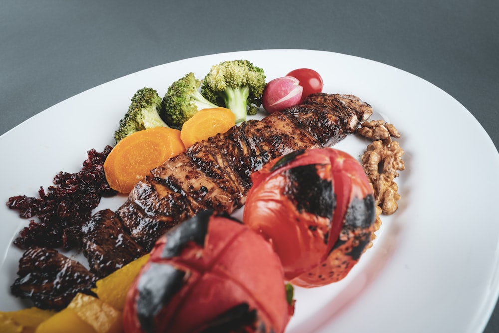 gegrilltes Fleisch mit geschnittenen Tomaten und grünem Gemüse auf weißem Keramikteller