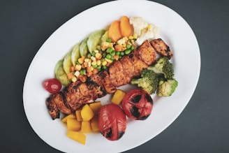 grilled meat with sliced lemon and sliced tomatoes on white ceramic plate