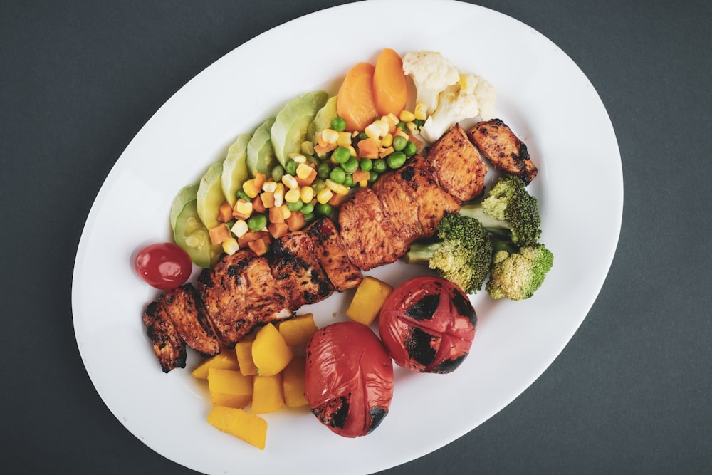 grilled meat with sliced lemon and sliced tomatoes on white ceramic plate