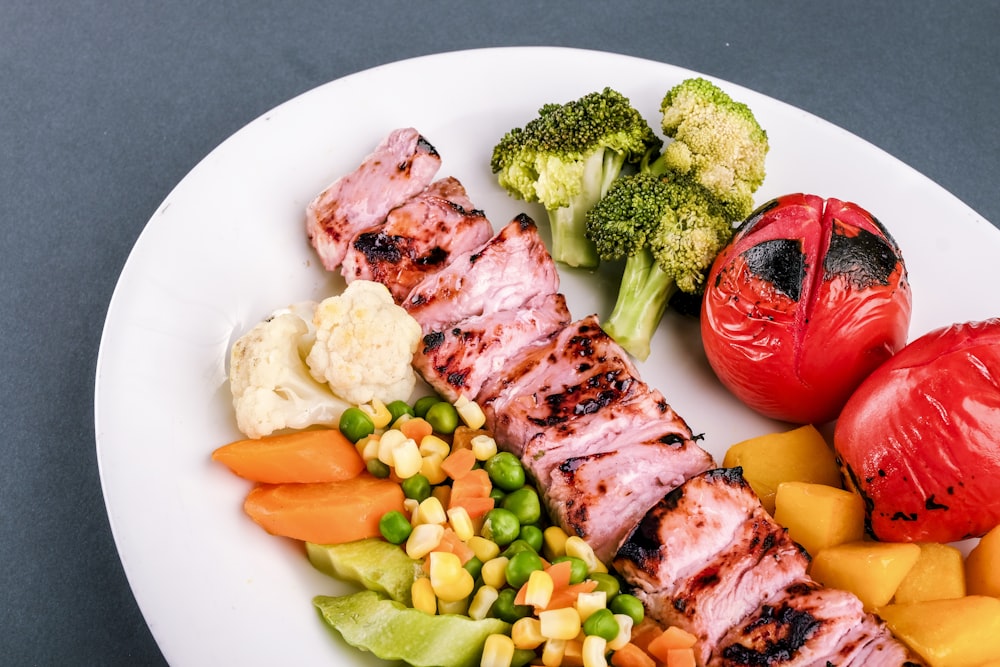 흰색 세라믹 접시에 녹색 야채와 붉은 고추를 곁들인 구운 고기