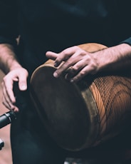 person in black shirt holding brown wooden drum