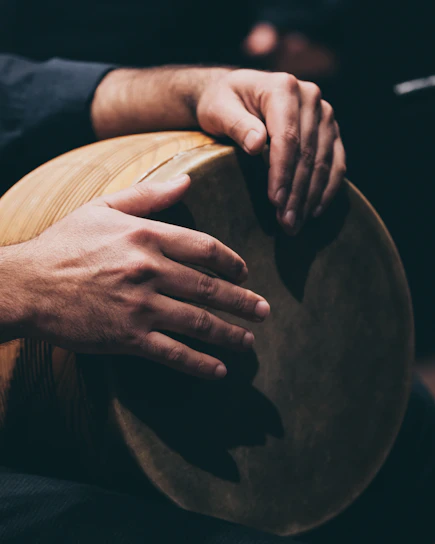 Close-up of an artisan’s hands skillfully shaping a Mandar drum’s wooden frame against a warm terracotta backdrop.