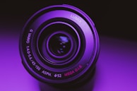 Close-up of a cinematic camera lens glowing with purple and electric green neon lights.