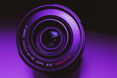Close-up of a sleek camera lens reflecting vibrant purple light.